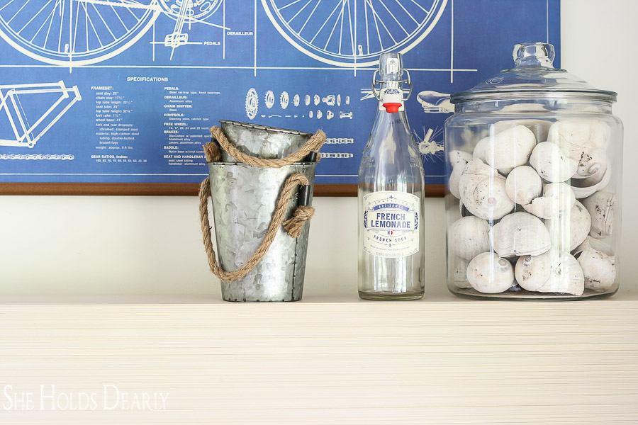Summer Farmhouse Decor with vintage bicycle poster, glass french lemonade bottle from World Market, galvanized buckets with rope handles and large glass jar with seashells