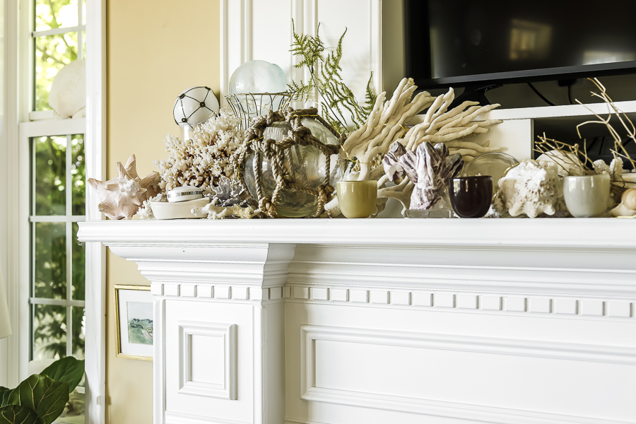 A fireplace mantle with nautical decorating including corals and shells and pops of green from mossy ferns.