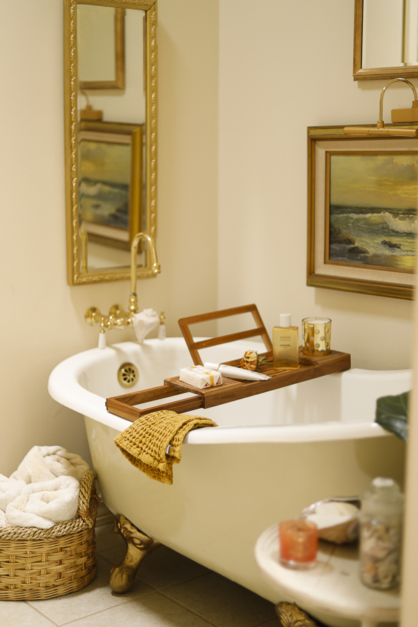 Beautiful claw foot slipper bath tub surrounded by nautical decorating. Gold framed art & a tall rectangular mirror hang on the surrounding walls.